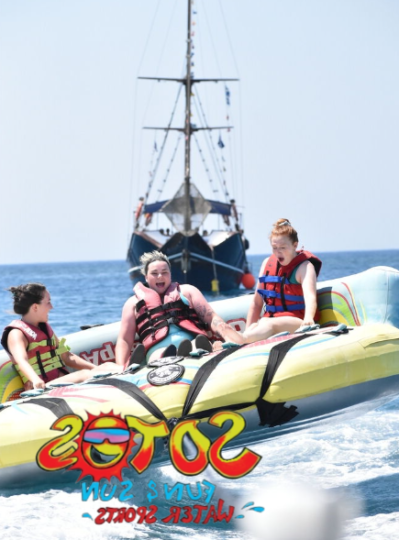 This picture shows 3 people on the inflatable ride of Crazy Ufo, in the back their is a boat and the sky is blue . In the face of the girls you can see the excitement and a little of fear